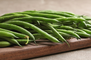 Wooden board with fresh green French beans on table, closeup