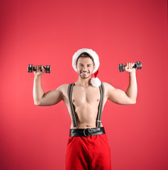 Shirtless sexy young Santa Claus with dumbbells on color background