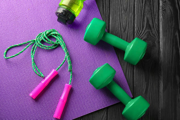 Yoga mat with jump rope and  dumbbells on wooden background
