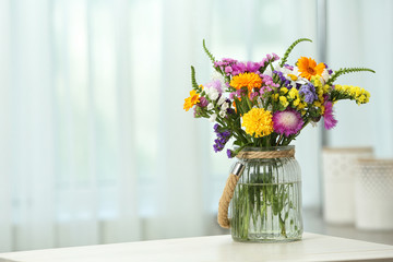 Vase with wild flowers on table against blurred background