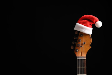 Guitar with Santa hat on black background. Christmas music concept