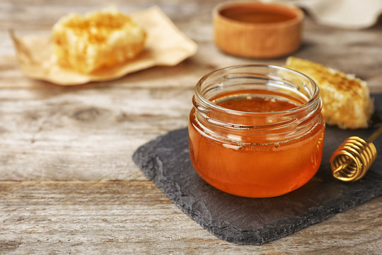 Glass jar with sweet honey and dipper on wooden table, closeup