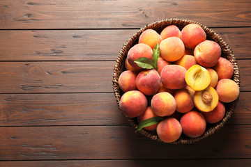 Wicker basket with fresh sweet peaches on wooden table, top view