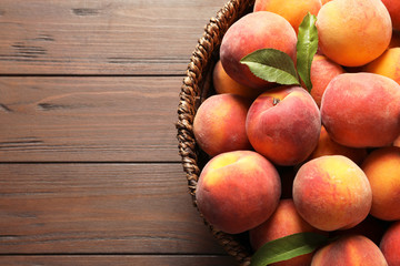 Wicker basket with fresh sweet peaches on wooden table, top view
