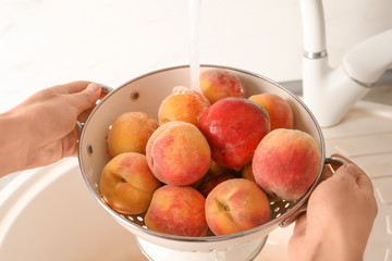 Woman washing fresh sweet peaches in kitchen