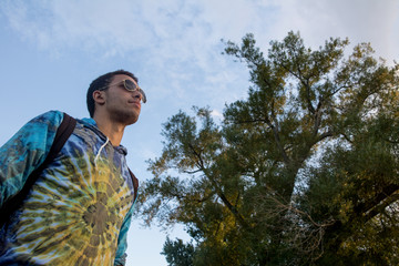waist up view of man wearing sunglasses looking into the distance in front of trees and sky - 214148296