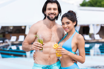 couple holding glasses of lemonades near swimming pool