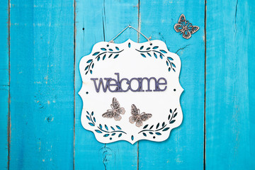 Welcome sign with floral border and butterflies hanging on antique rustic teal blue wooden background