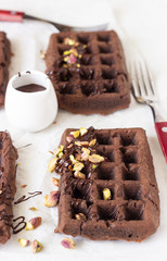 Chocolate belgian waffles decorated with melted chocolate and pistachios on a white paper.