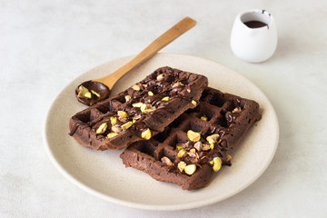 Chocolate belgian waffles decorated with melted chocolate and pistachios on a plate and light background.