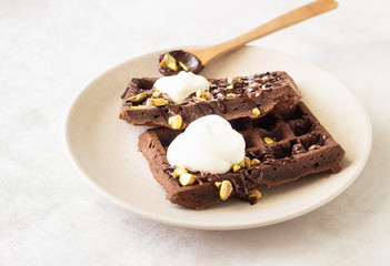 Chocolate brussels waffles decorated with melted chocolate, pistachios and whipped cream on a plate.
