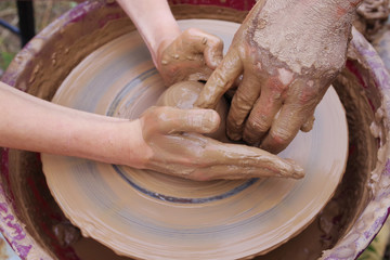 Potter's hands and the child's hand in clay over a potter's wheel. A master class on production of pottery. Modeling of clay on a potter's wheel