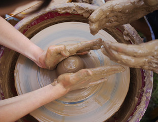 Potter's hands and the child's hand in clay over a potter's wheel. A master class on production of pottery. Modeling of clay on a potter's wheel