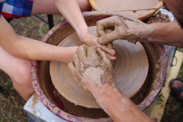 Potter's hands and the child's hand in clay over a potter's wheel. A master class on production of pottery. Modeling of clay on a potter's wheel