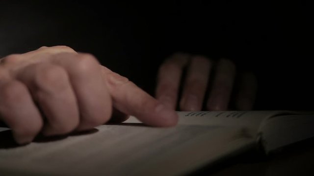 Close-up of a man's hand holding an open paper book, turning the pages with his fingers