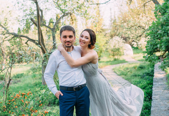 A loving couple is walking in a blooming garden. Red-haired girl in a modest, gray dress in rustic...