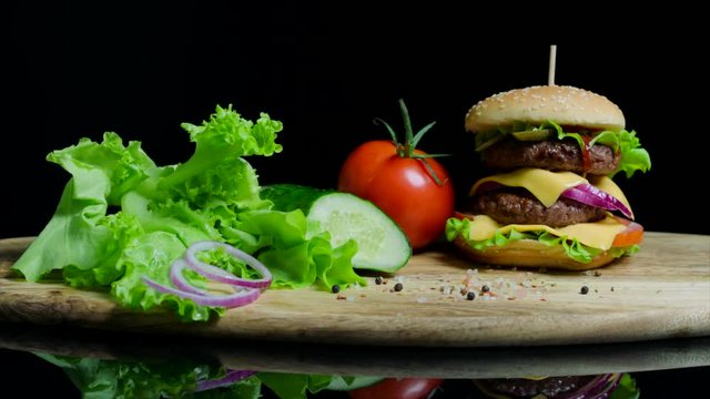 Fresh vegetables and tasty burger with cheese and beef cutlets on the black background