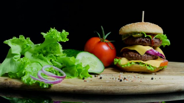 Fresh vegetables and tasty burger with cheese and beef cutlets on the black background