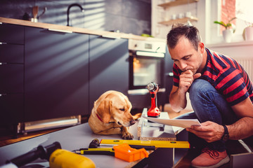 Man with dog checking blueprints while building kitchen cabinets