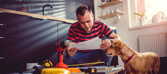 Man with dog checking blueprints while building kitchen cabinets