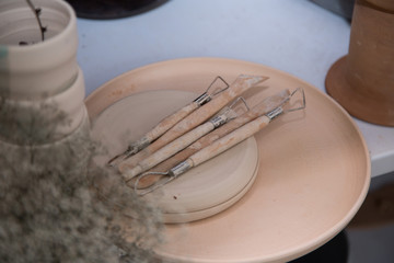 Pottery tools like loops and knives on raw ceramic plates in a pottery workshop
