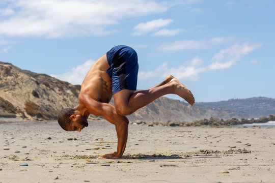 Athletic man at the beach in Crow yoga pose