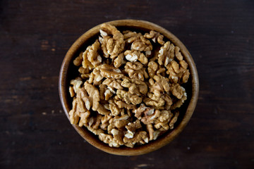 A wooden bowl of walnuts on a dark wooden background top view