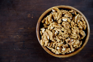 A wooden bowl of walnuts on a dark wooden background top view
