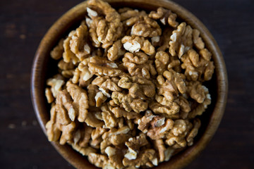 A wooden bowl of walnuts on a dark wooden background top view
