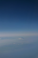 Naklejka na ściany i meble Defocus, abstract and dreamlike photo of Mount Fuji from the sky among sea of clouds in blue shade, shoot from airplane. Very soft, sweet and subtle. Blurred.