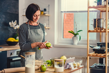 Woman peeling apples in the kitchen - obrazy, fototapety, plakaty