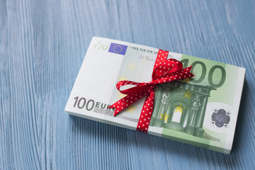 A stackof euro bills with a red ribbon bow on a blue wooden background