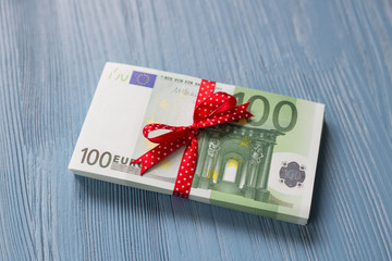 A stackof euro bills with a red ribbon bow on a blue wooden background