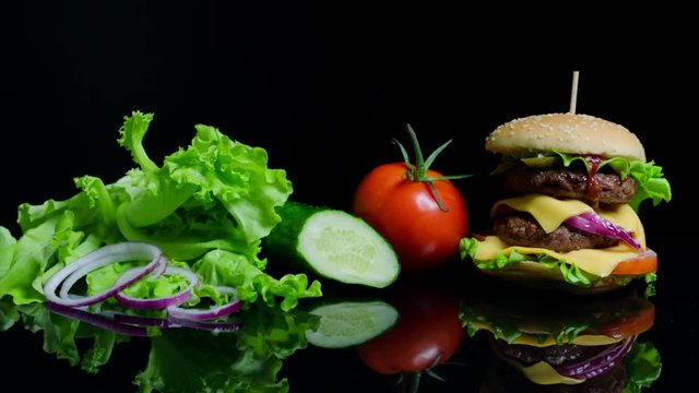 Fresh vegetables and tasty burger with cheese and beef cutlets on the black background