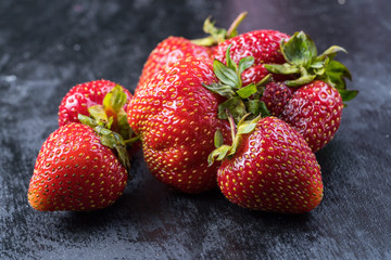 Fresh red strawberry on black stone plate in dark background.