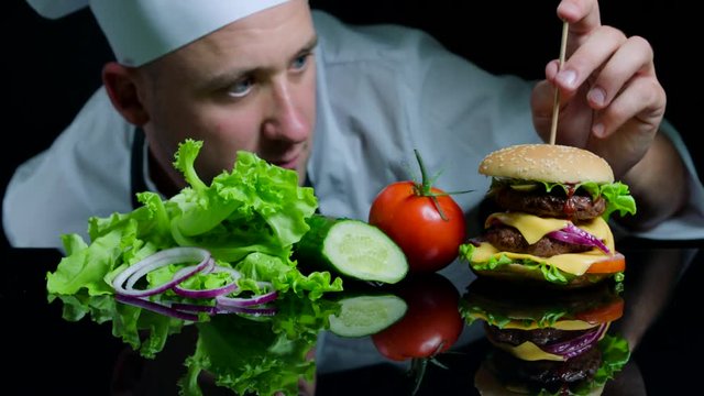 Chef finishing the savory burger with beef, cheese and vegetables. Black background for commercial
