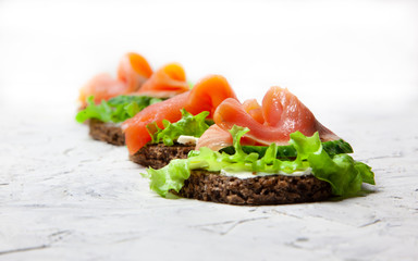  Sandwich with salmon. Subject photography, food shooting. Juicy lettuce leaves and fresh cucumber, a slice of tender red fish on black bread.