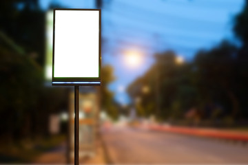 Vertical blank glowing billboard on the night city street. In the background buildings and road with cars. Mock up. The poster on the street next to the roadway.