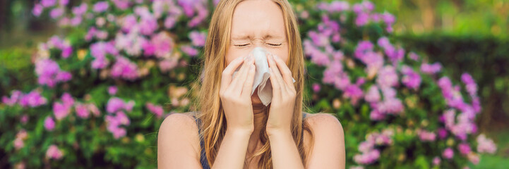 BANNER Pollen allergy concept. Young woman is going to sneeze. Flowering trees in background long...
