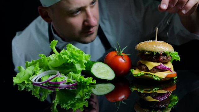 Chef finishing the savory burger with beef, cheese and vegetables. Black background for commercial