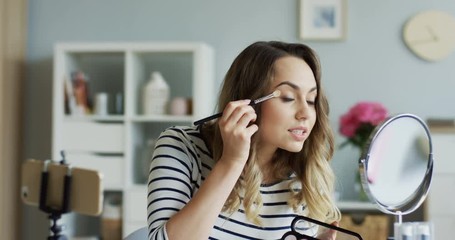 Young pretty woman shooting beauty blog video and doing makeup for eyes. Close up. Inside.