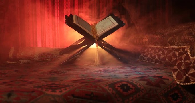 Open holy book of Muslims on stand on eastern carpet with dark toned foggy background. Muslim religion concept. Selective focus. Slider shot.