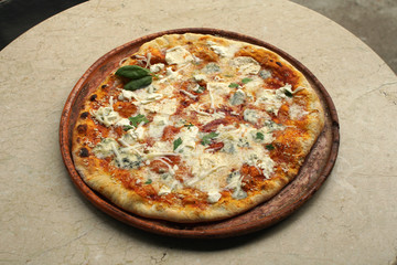 Cheesy pizza on a restaurant marble table. Basil leaves, tomato sauce, ham