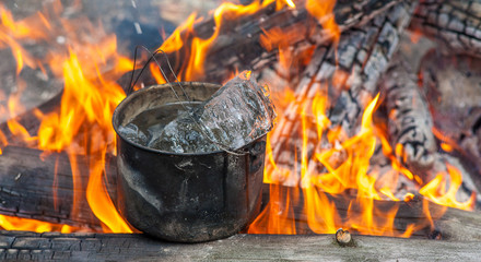 Cooking in the nature. Cauldron with ice on fire in forest. Kitchen in travel.