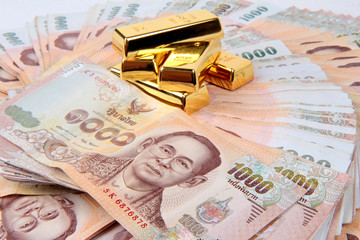 5 of 1 kg. Gold bar on 1000 Baht of Thailand banknotes nested a pile high.