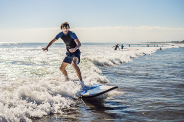 Young man, beginner Surfer learns to surf on a sea foam on the Bali island
