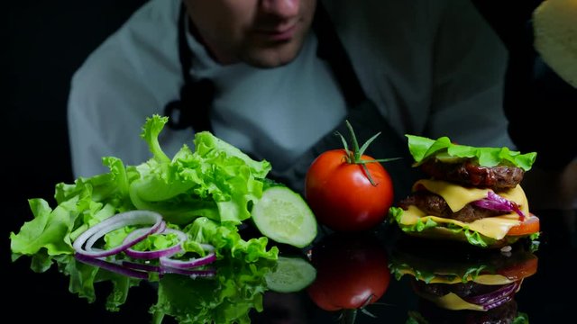 Chef finishing the savory burger with beef, cheese and vegetables. Black background for commercial