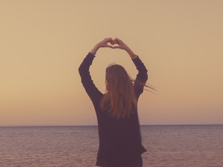 Girl holding heart shape in the sunset / sunrise time.