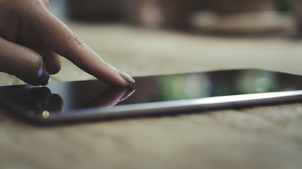 Closeup image of woman's finger pointing at a tablet pc on wooden table