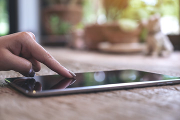 Closeup image of woman's finger pointing at a tablet pc on wooden table